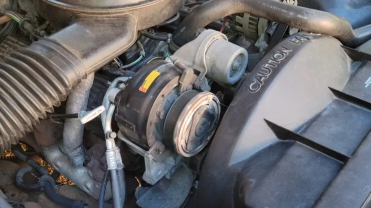  an automotive engine bay focusing on the air conditioning (AC) compressor