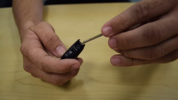 Close-up of hands using a key to pry open a Toyota key fob, demonstrating the process of changing the battery