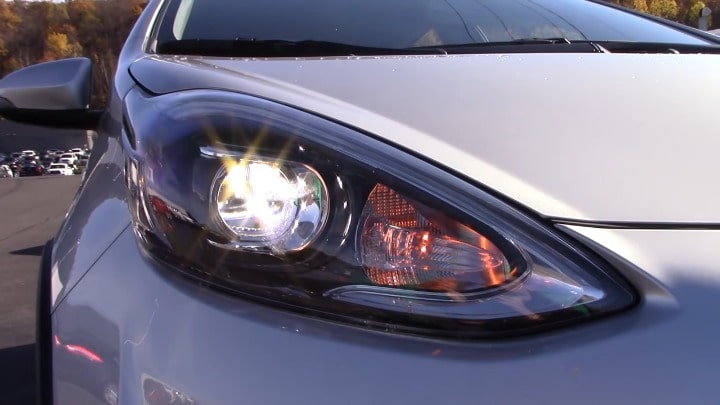 Close-up of the headlight of a Toyota Prius C, showcasing the sleek, modern design of the front light assembly on a silver model