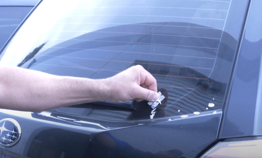 A guy is holding razor in his hand and is scraping sticker of the car window