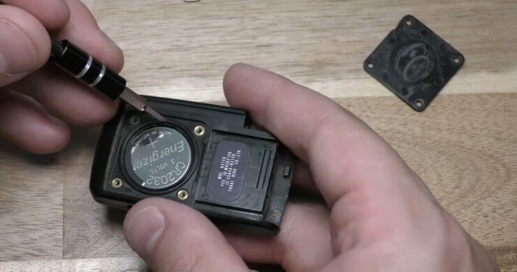 person using a small tool to remove a CR2032 battery from a Toyota key fob during a battery replacement process