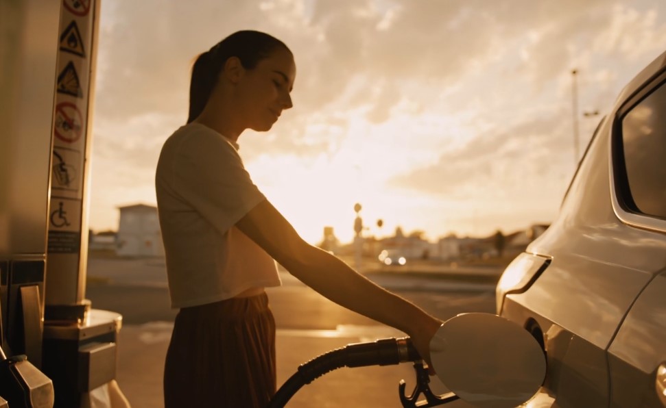 Woman fueling her car at a gas station during sunset