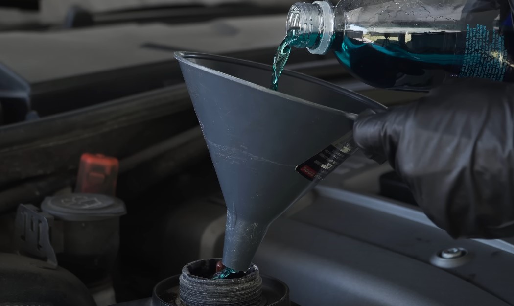 Close-up of pouring a teal-colored coolant in car's radiator