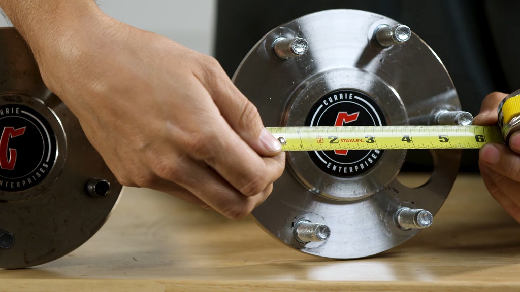 A man measuring a bolt pattern with a measuring tape