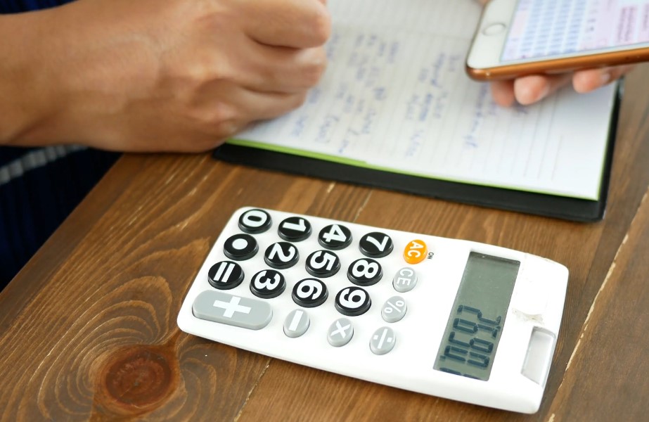 Person using calculator, with notepad and phone next to it