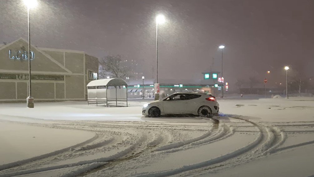 A white car navigates a snowy parking lot at night