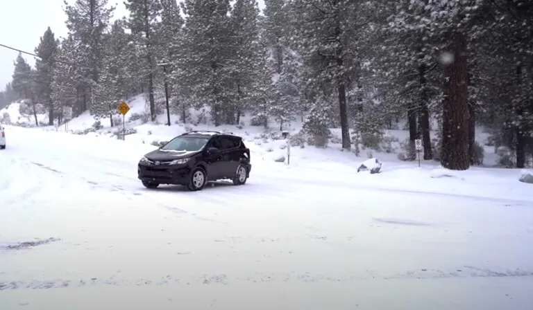 Snow-covered roadway; a car moves cautiously through the wintry landscape