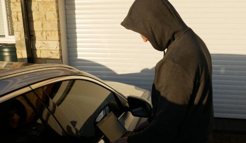 A thief in a hoodie stealing a car