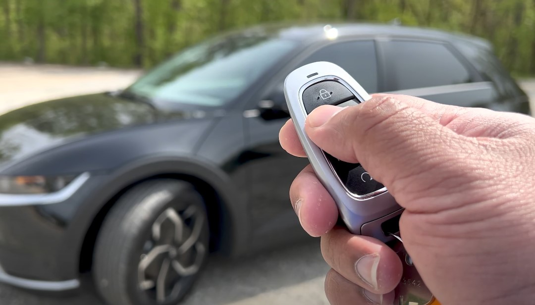 A hand holds a modern car key fob, ready to unlock a black SUV