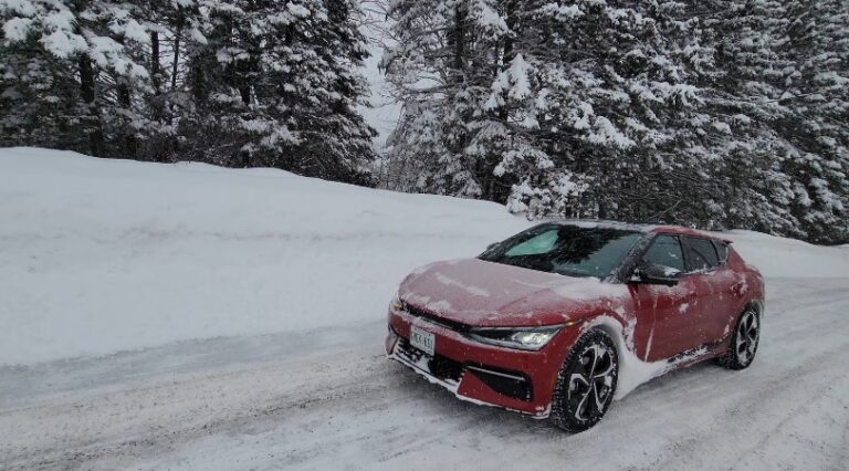 A red electric car navigates a snowy mountain road, its path clear amidst the pristine white landscape