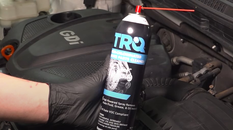 A person holding a can of trro, positioned in front of a car engine