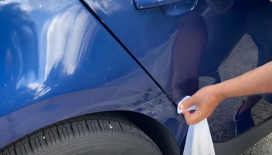 A person cleans a section of a dark blue car