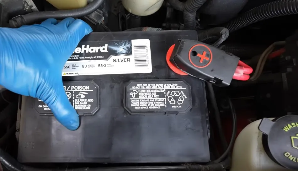 A person replacing a dead car battery wearing blue gloves
