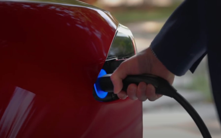 A hand inserts a charging cable into a red electric vehicle