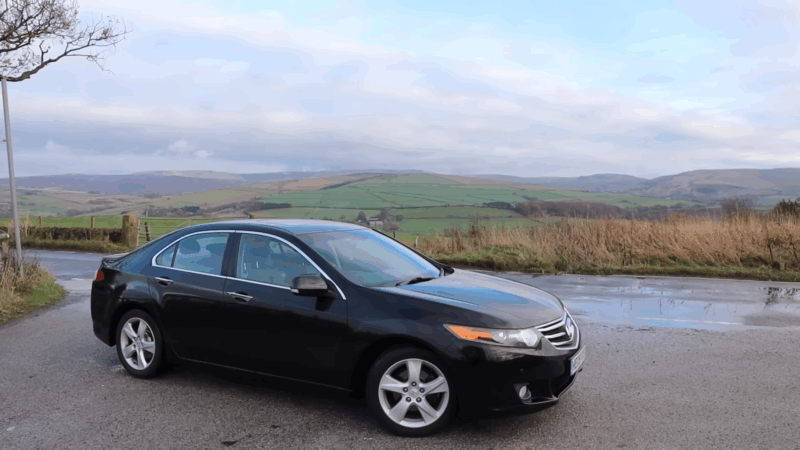 A black Honda Accord sedan parked on a country road with hills in the background