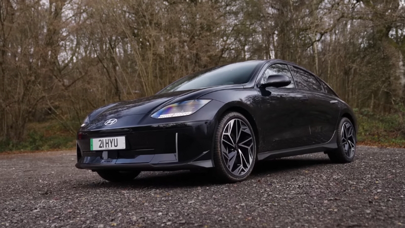 A black Hyundai Ioniq 6 parked on a forest road with trees in the background