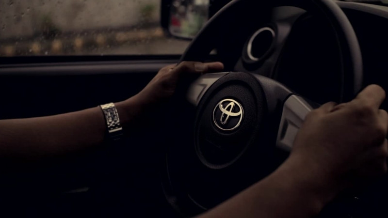 Person driving a Toyota car, focusing on the steering wheel with rainy weather visible outside