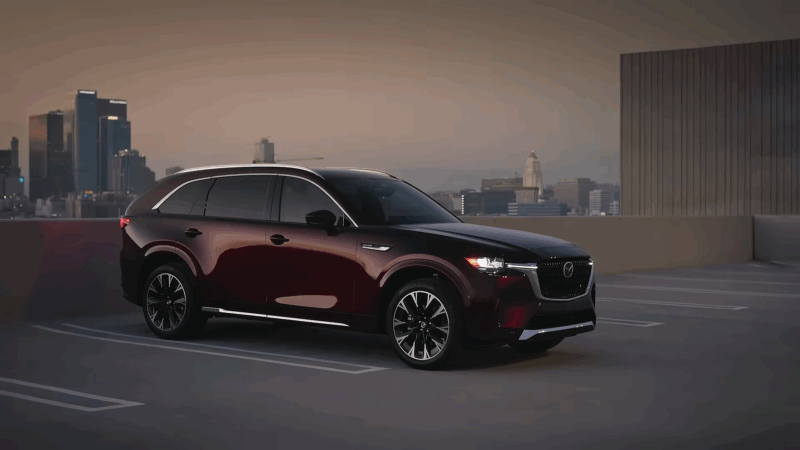 A dark red Mazda CX-90 parked on a rooftop with a city skyline in the background