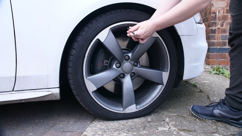 Person checking the air pressure of a car tire using a gauge