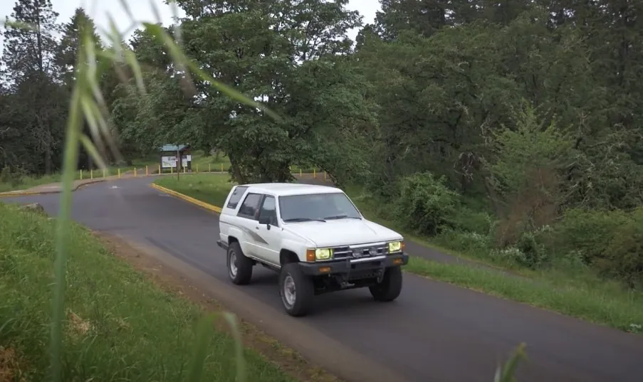 A white 4Runner SUV navigates a winding road through a lush forest