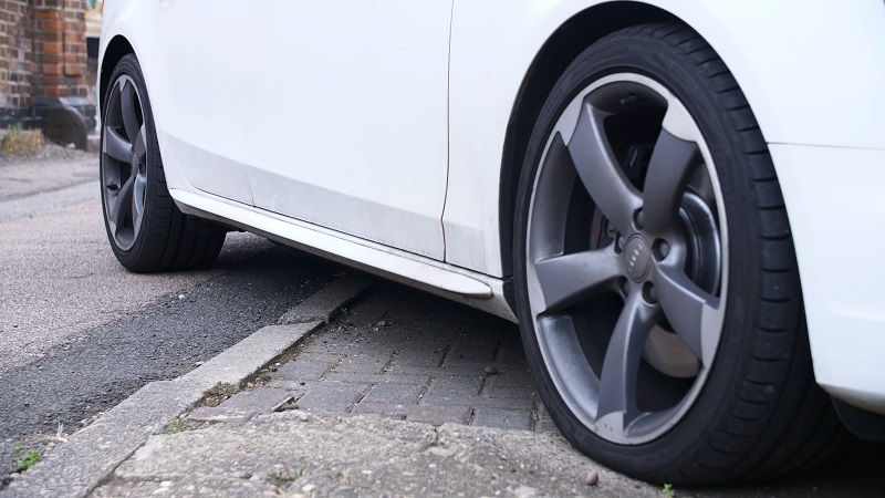 Low-angle view of mismatched tires on a white car parked at a curb