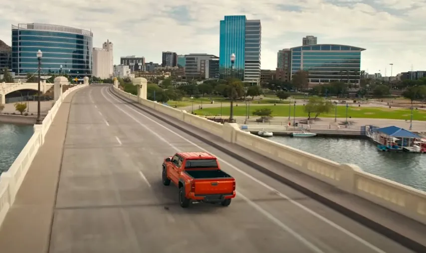 An orange Tacoma pickup truck navigates a city bridge