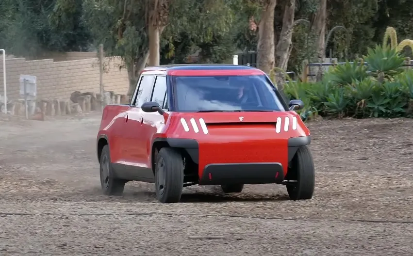 A vibrant red Telo MT1 pickup truck, navigating a dusty gravel road