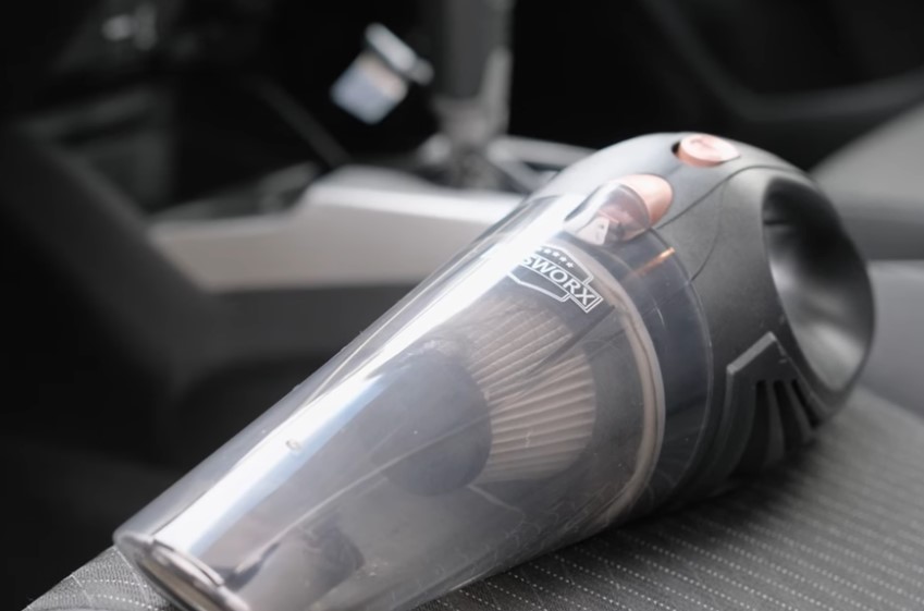 A compact, handheld vacuum cleaner rests on a car seat