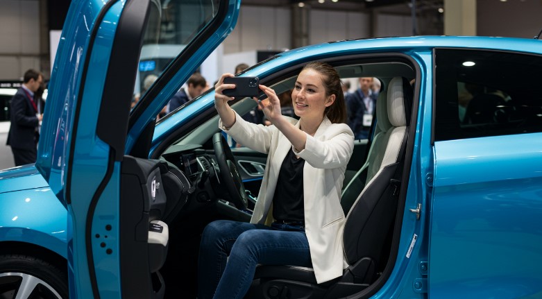 A smiling woman takes a selfie in a modern vehicle at an auto show