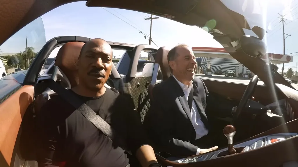 Jerry Seinfeld and Eddie Murphy driving a convertible sports car, enjoying casual conversation on this unique blend of comedy and cars