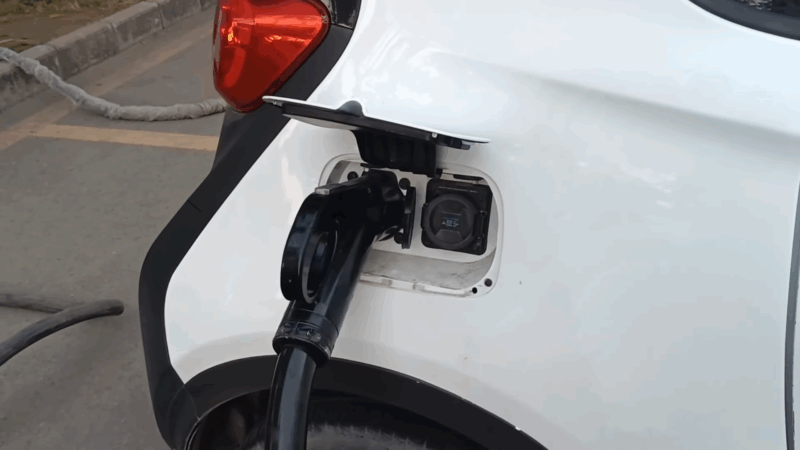 Electric car plugged into a charging port with the cover open on a city street