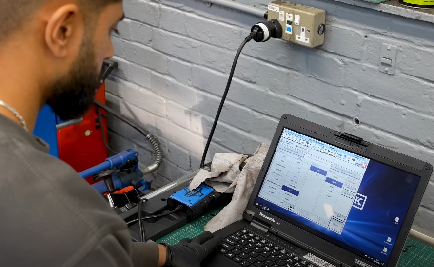 A car mechanic running electric vehicle diagnostics on a laptop