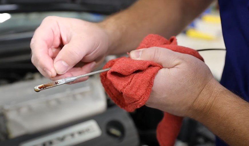 A close-up of the oil dipstick being cleaned with a red rag
