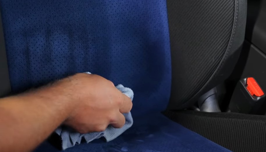 A light-blue cloth gently wipes away dirt and grime from a dark-blue car seat