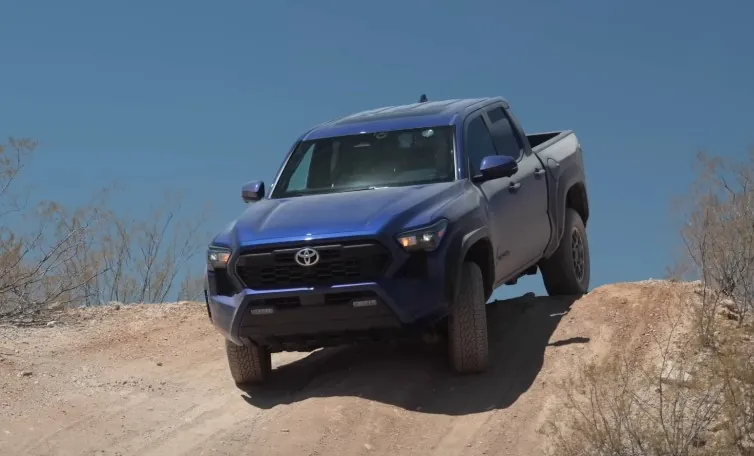 Blue Toyota Tacoma ascends a sandy incline