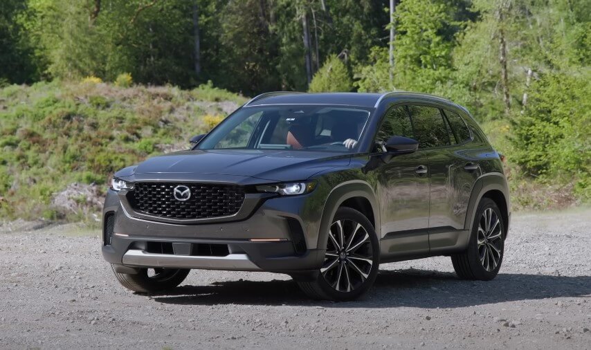 A gray Mazda CX-50 SUV navigates a gravel road,