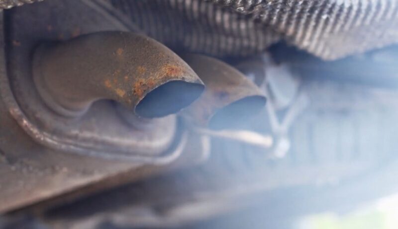 Exhaust fumes billowing from rusted car tailpipes