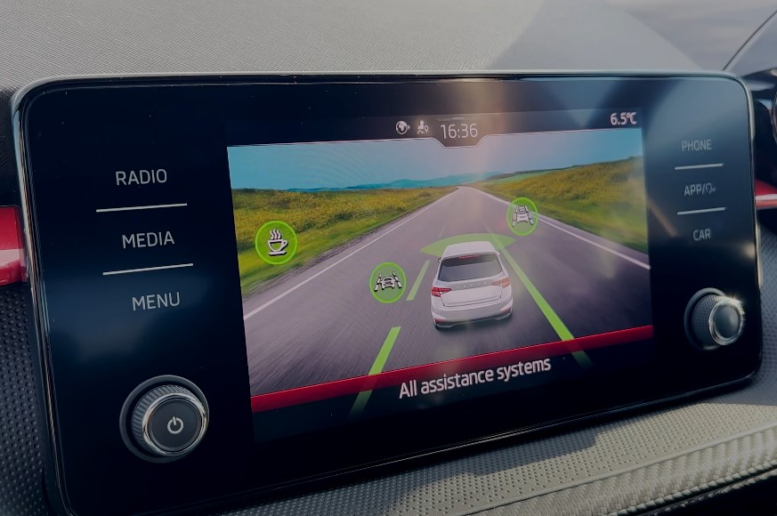 Modern car dashboard displays a live view of the road ahead, with various assistance systems highlighted