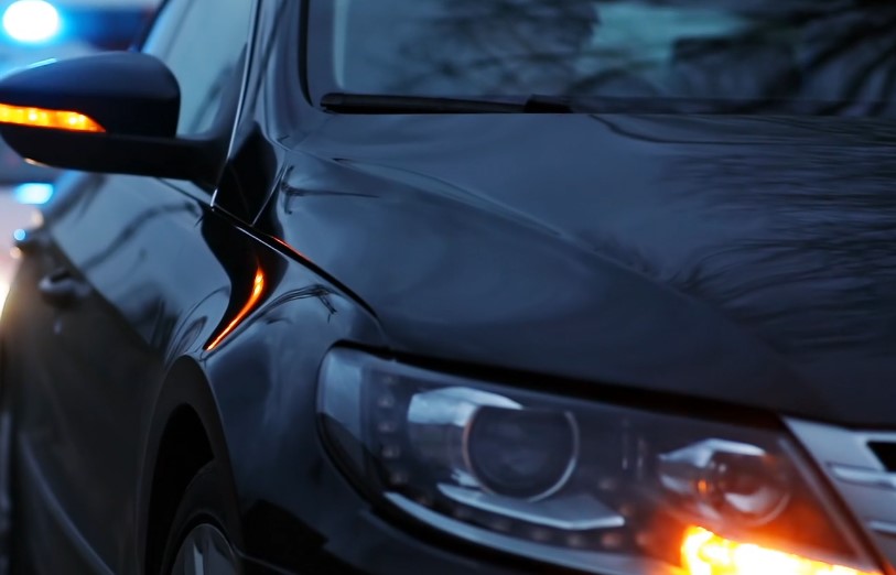 A dark vehicle, likely a car, is positioned in a police-involved situation