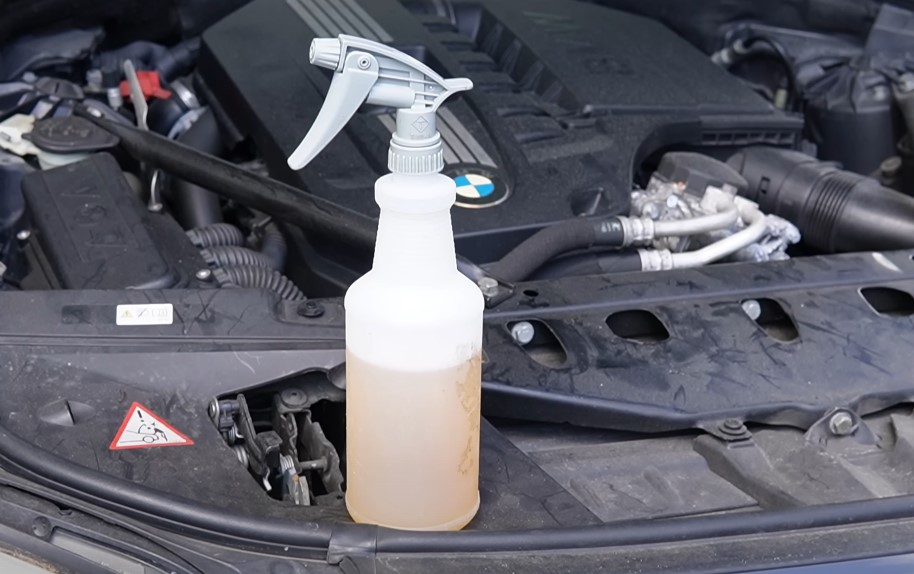 A bottle of car cleaner placed on top of a car engine