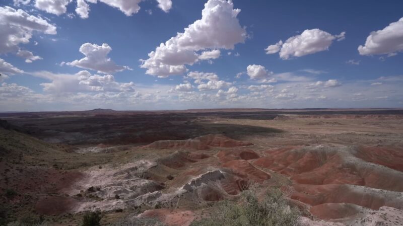 Expansive desert view of the Painted Desert along historic Route 66 under a blue sky with scattered clouds.