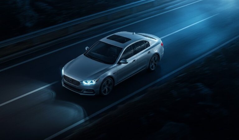 A sleek silver sedan glides along a dark highway, its headlights illuminating the road ahead