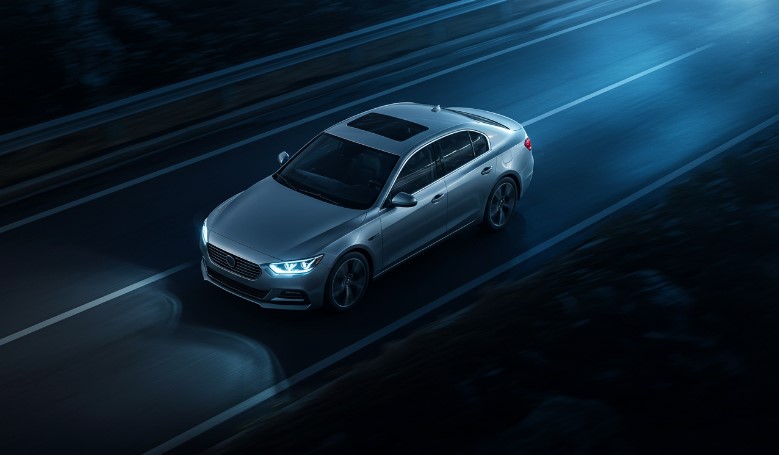 A sleek silver sedan glides along a dark highway, its headlights illuminating the road ahead