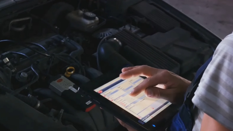 A mechanic uses a diagnostic tablet to check a car’s charging system after an alternator replacement