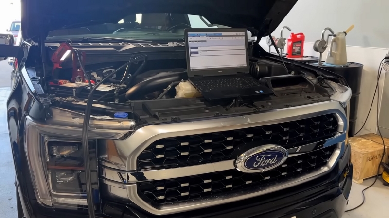 A Ford truck with the hood open and a diagnostic laptop connected