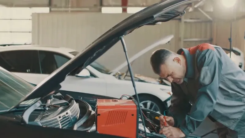 A mechanic checks a car engine with the hood open, testing connections despite a new alternator installed