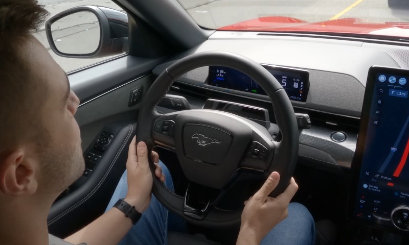 A man drives a car, focusing on a digital screen displayed on the dashboard