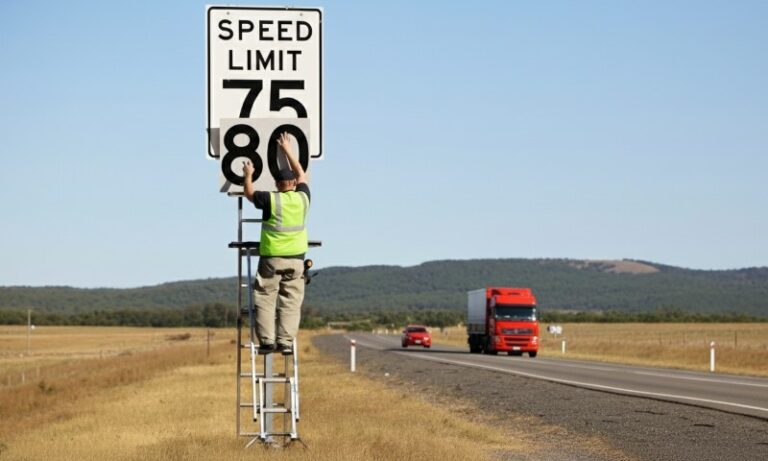 A man on a ladder adjusts a speed limit sign, ensuring proper visibility for drivers on the road