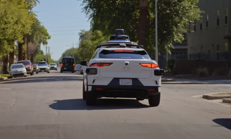 A self-driving car moving on a road, with urban elements like sidewalks and traffic signs visible