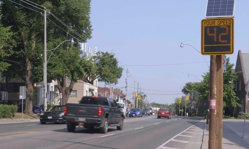 A street scene with cars driving and a visible speed limit sign indicating traffic regulations